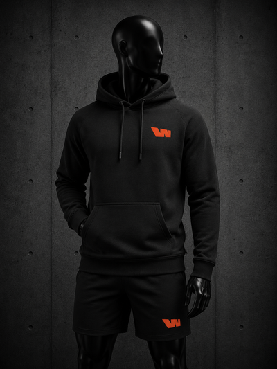 A black hoodie and matching black shorts set displayed on a glossy black mannequin against a dark textured wall. The hoodie features a small orange logo on the left chest, and the shorts feature a matching orange logo on the left thigh.