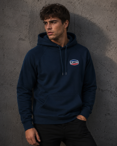 Man wearing a navy blue hoodie with a logo against a gray concrete wall