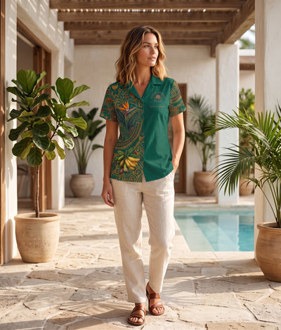 A woman stands in a sunlit outdoor patio corridor beside a pool, wearing a short-sleeve collared button-up shirt with a green base and multicolor tropical floral and paisley print, paired with cream pants and brown sandals.
