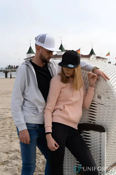 Two people in hoodies and caps on the beach with Premium American Twill pro sticker